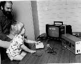 Dr Harvey Cohen supervises two-year old
 Alexander Zeno Cohen operating +- keyboard
 1975 microcomputer. Monitor is adapted TV